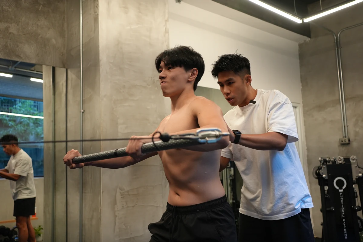 Taka 教練在一旁觀察並引導學員做橫桿動作